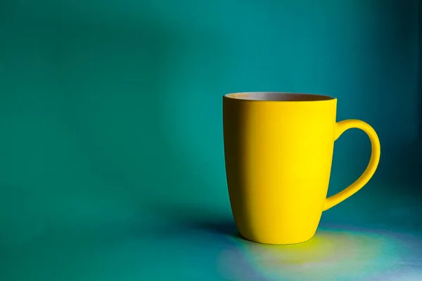 Yellow mug against a blue background in natural light - contrasting photo with space for writing text