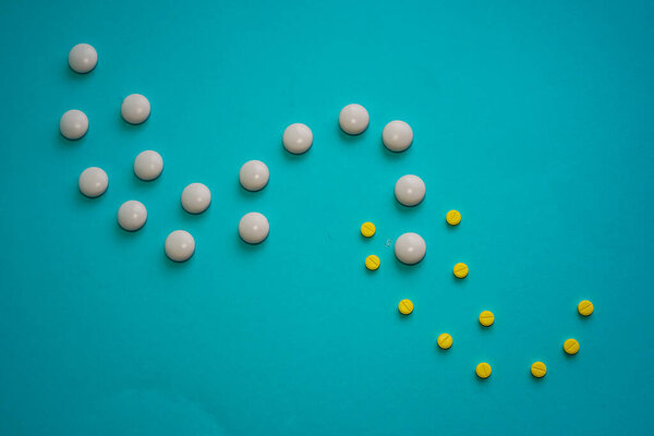Yellow and white round pills laid out in the form of a wave on a diagonal photo on a blue background