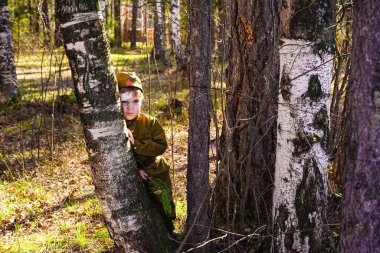Büyük Zafer Günü 'nden önce ormanda üniformalı bir çocuk. Kalplerimizde 2. Dünya Savaşı. Şapkalı çocuk ve doğada tunik.