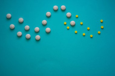 Sarı ve beyaz yuvarlak haplar, mavi arka plandaki bir fotoğrafın tepesine bir dalga şeklinde serilmişti.
