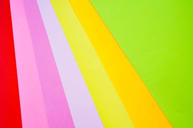Parlak renkli ofis kağıtları beyaz arka planda yukarıdan yakın plan çekilir. Kırmızı, pembe, mor, sarı, turuncu, yeşil