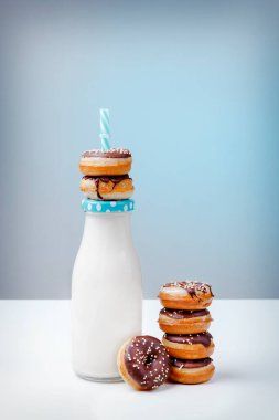 50. caddeye dön. Lezzetli, aromalı mini çörekler, beyaz masa ve mavi arka plan ışığı üzerinde bir şişe sütle..