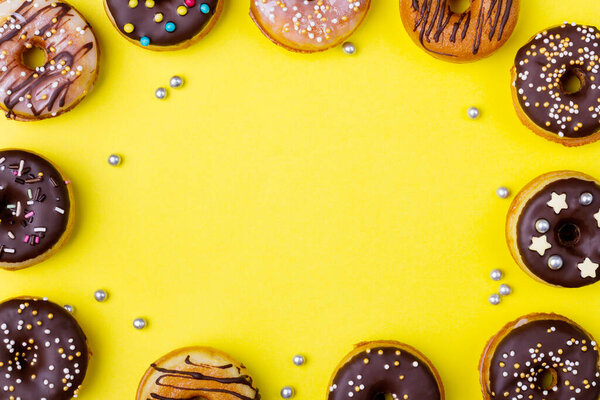 Yummy glazed assorted three doughnuts on pastel yellow background. Top view. Copy space in center.