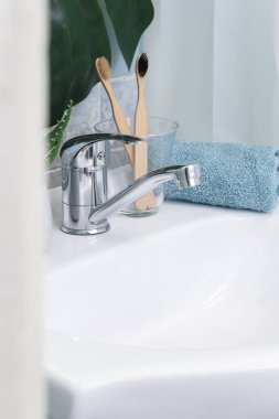 Sıfır atık banyo. Eko doğal bambu diş fırçaları, mavi havlu ve lavabonun üzerinde sulu. Arka planda yeşil palmiye yaprağı var. Boşluğu kopyala