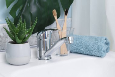 Sıfır atık banyo. Eko doğal bambu diş fırçaları, mavi havlu ve lavabonun üzerinde sulu. Arka planda yeşil palmiye yaprağı.