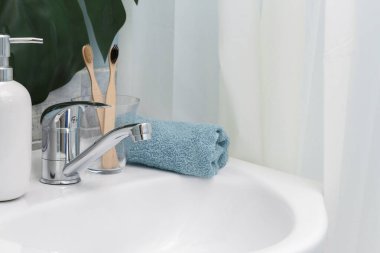 Sıfır atık banyo. Eko doğal bambu diş fırçaları, mavi havlu ve lavabonun üzerinde sulu. Arka planda yeşil palmiye yaprağı.