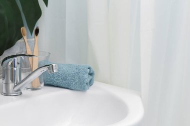 Sıfır atık banyo. Eko doğal bambu diş fırçaları, mavi havlu ve lavabonun üzerinde sulu. Arka planda yeşil palmiye yaprağı var. Boşluğu kopyala