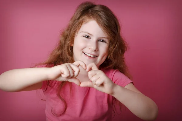 Redhead curly cute girl child showing heart hands. Close up portrait. Love, positive feeling and emotion