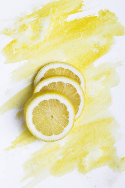 Top view of three lemon pieces on white paper with yellow watercolor