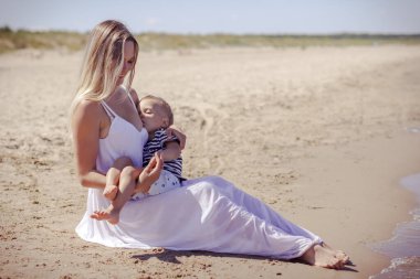 Anne sahilde bebeğini emziriyor, denizde sarılıyor, plajda dinleniyor. 