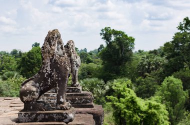 İki tahrip edilmiş taş aslan Kamboçya 'daki Angkor Wat arkeoloji parkındaki Pre Rup tapınağının üst terasını koruyor..