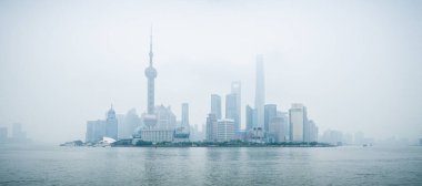 SHANGHAI, ÇİN - 6 HAZİRAN 2015: Çin 'in Şangay kentindeki Huangpu nehrinin karşısından iş bölgesinin yüksek binaları ve kuleleri bir kirlilik sisinin arkasında beliriyor.
