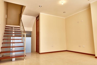 Tahta merdiven boş oturma odasına basar.