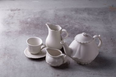 Çaydanlık kreması, fincan ve çay tabağı çimento tahtasında..