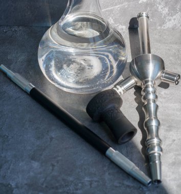 Çelik nargile matarası, ağızlık ve kil kasesi, gri beton arka planda tütün..