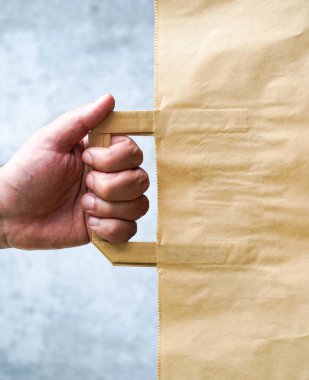 İnsan eli mavi arka planda bir kese kağıdını elinde tutar. Kraft çantası elini tutuyor. Ekolojik kağıt alışveriş torbası adamın elinde. Boşluğu kopyala