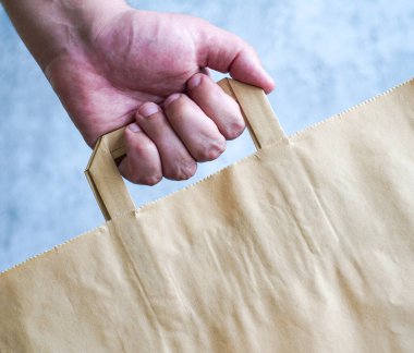 İnsan eli mavi arka planda bir kese kağıdını elinde tutar. Kraft çantası elini tutuyor. Ekolojik kağıt alışveriş torbası adamın elinde. Boşluğu kopyala