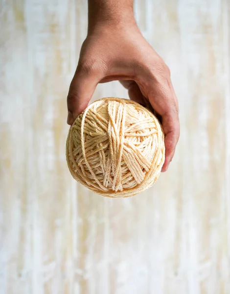 Male hand holding a ball of thread of color natural wool on a wooden background. Hobbies copy space flat lay