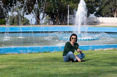 Bulanık doğa geçmişi olan genç, rahat bir kadın. Çeşmenin yanındaki parkta yürüyen güzel kız.