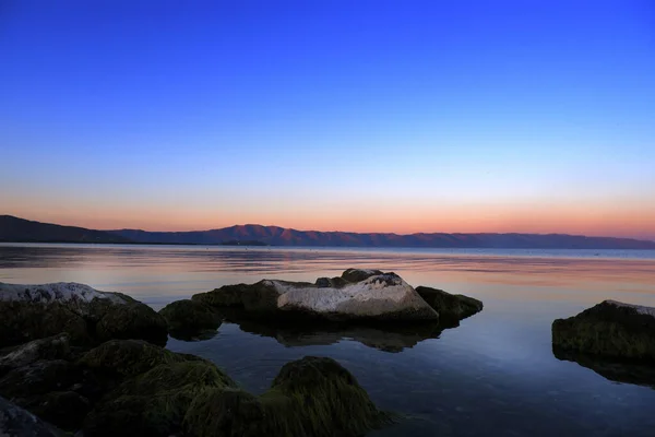 Gölün üzerinde gün batımı ve suda büyük yosunlu taşlar, ufukta dağlar -- günbatımı deniz manzarası, arka plan. Sevan Gölü. Ermenistan. Barışın sükuneti kavramı