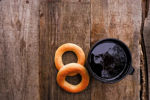 Fresh poppy bagel and hot thermo tea or coffee mug on a rustic brown wooden table. Breakfast or snack time. Top view with copy space. Camping food. Wood background