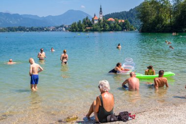 Bled, Slovenya - 10 Ağustos 2019: İnsanlar arka planda Bled Gölü kıyılarında dinleniyor Slovenya 'da küçük bir adada kilisenin bulunduğu güzel bir manzara