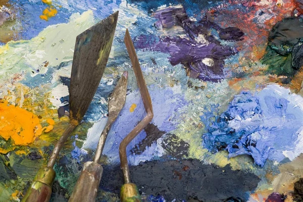 Well used artists palette knives on a multi-coloured paint palette
