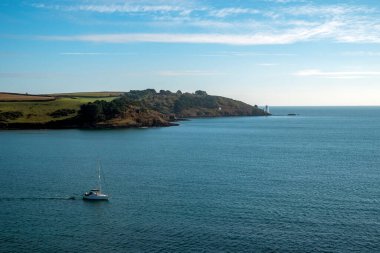 Bir yelkenli St. Anthony Head 'den ve St. Mawes, Cornwall, İngiltere' den görülen deniz fenerinden geçiyor.