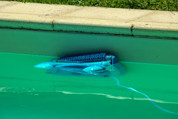 Otomatik bir robot havuz temizleyicisi bulutlu bir yüzme havuzunun kenarına tırmanıyor ve enkaz ve yosunları temizliyor.