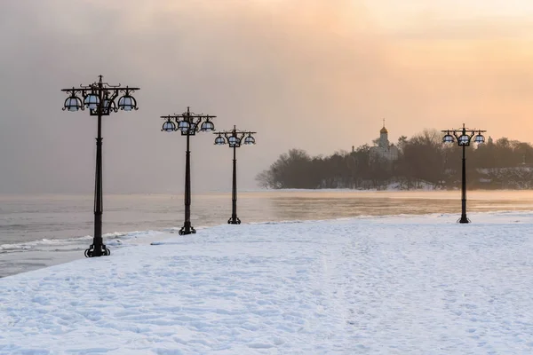 Terraplén nevado a lo largo del río brumoso con linternas en el amanecer brumoso paisaje de invierno. Yo... — Foto de Stock