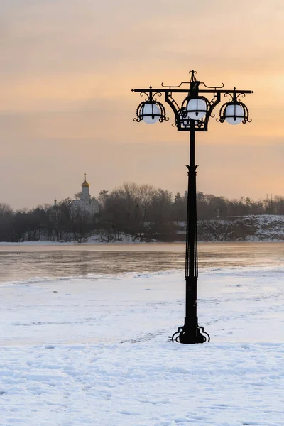 Besneeuwde dijk langs de mistige rivier met lantaarns op het mistige sunrise - winterlandschap. III — Stockfoto