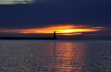 Ufuktaki deniz fenerinin güzel manzarası gün batımında turuncu bir gökyüzünün arka planına karşı