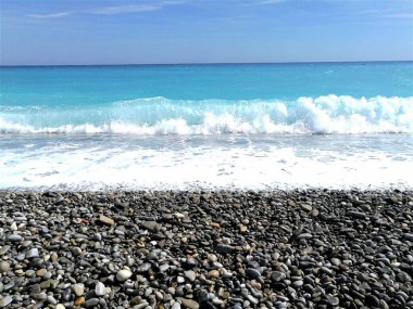 Deniz kıyısında. Gök mavisi su ve çakıl