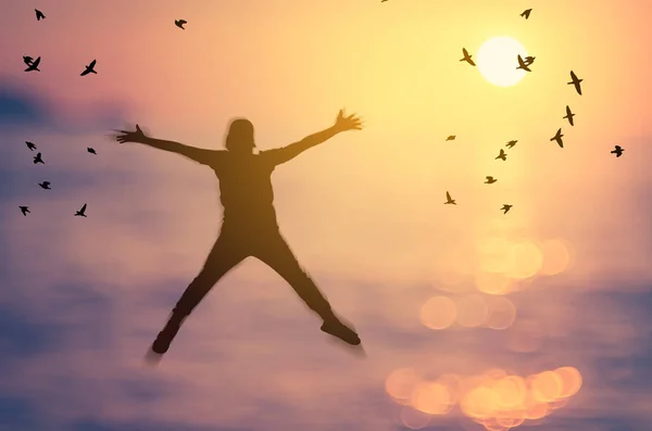 Libertad y sentirse bien concepto. Copiar el espacio de silueta feliz hombre saltando en borrosa playa de atardecer tropical con aves volar fondo abstracto . — Foto de Stock