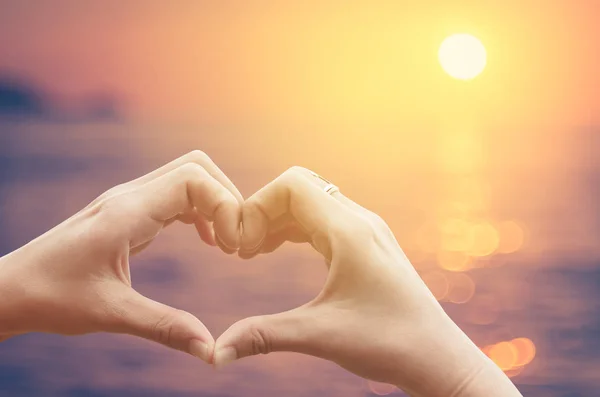 Vrouwelijke handen hart vorm op natuur bokeh zon licht flare Golf en tropisch strand abstracte achtergrond wazig. — Stockfoto