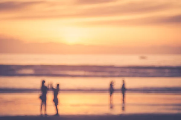 Blur people relax on tropical sunset beach with bokeh sun light wave abstract background. — Stock Photo, Image