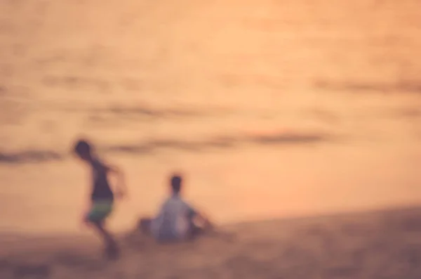 Blur crianças brincando na praia tropical do por do sol com bokeh sol luz onda abstrato fundo . — Fotografia de Stock