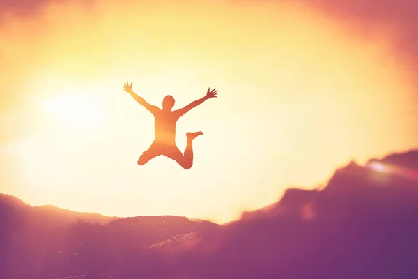 Glücklicher Mann springt auf dem Gipfel des Berges mit Sonnenuntergang Himmel abstrakten Hintergrund. — Stockfoto