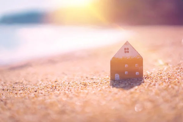 Small home model on sunset beach sand texture background.