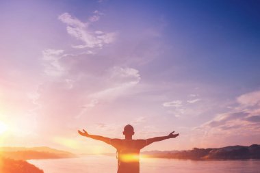 Mutlu sırt çantalı adam, gün batımında gökte nehir kenarında el kaldırsın.. 