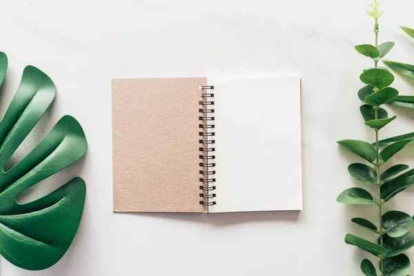 Tropical green leaf and notebook on white marble texture abstract background. — Stockfoto