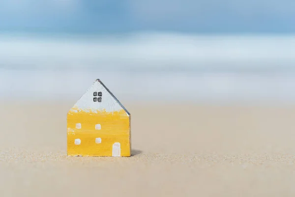 Pequeño modelo de casa en la playa de arena con fondo azul cielo . — Foto de Stock