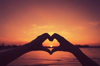 Kadın elleri doğada kalp şeklinde bokeh güneş ışığı dalgası ve tropik tropik günbatımı plaj soyut arka planı. Mutlu aşk yolculuğunun ve doğa konseptindeki özgürlüğün kopyası. Klasik ton rengi.