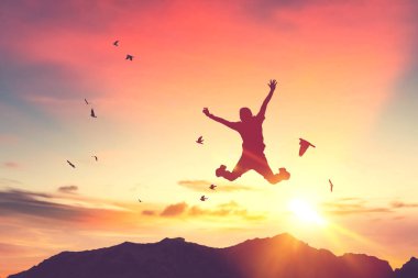 Siluet adam zıplıyor ve kuşlar gün batımında gökyüzünde uçuyor ve soyut arkaplan dokusunu bulutlandırıyor. İyi hissetme özgürlüğü ve seyahat macerası konseptini kopyala. Klasik ton filtre efekti renk biçimi.