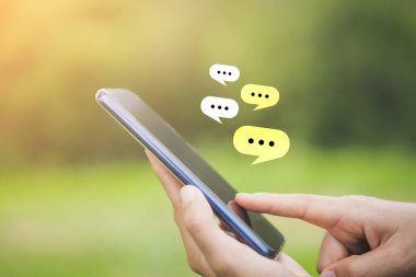 Açık doğa parkı arka planında sohbet ikonu olan akıllı bir telefon kullanarak kadın el ele tutuşunu kapat. Teknoloji ve seyahat tatil konseptinin kopyalama alanı. Klasik ton filtre efekti rengi.