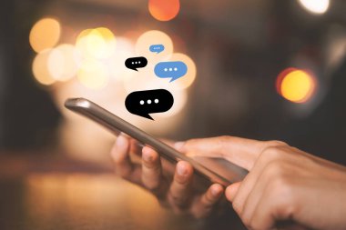 Kadın eli, kafenin soyut arka planında sohbet ikonu grafiği olan akıllı telefon kullanıyor. Teknoloji sektörü ve serbest meslek kavramı. Klasik ton filtre efekti renk biçimi.