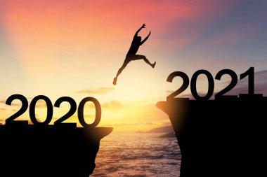 2020 'den 2021' e tropikal günbatımı plajında uçurumun arasında siluet adam zıplıyor. Özgürlük mücadelesi ve seyahat macera tatili konsepti. Klasik ton filtre efekti renk biçimi.