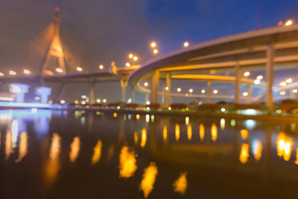 Night blurred bokeh suspension bridge with river reflection at twilight — Stock Photo, Image