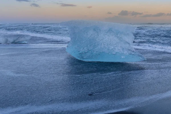 夕焼け空の背景の黒い砂のビーチに壊れる氷 — ストック写真