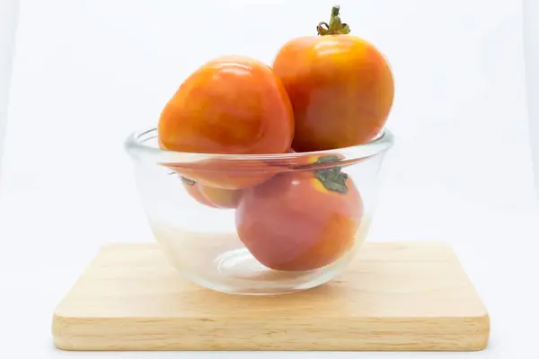 Tomate fraîche sur un bol en verre sur une planche en bois — Photo